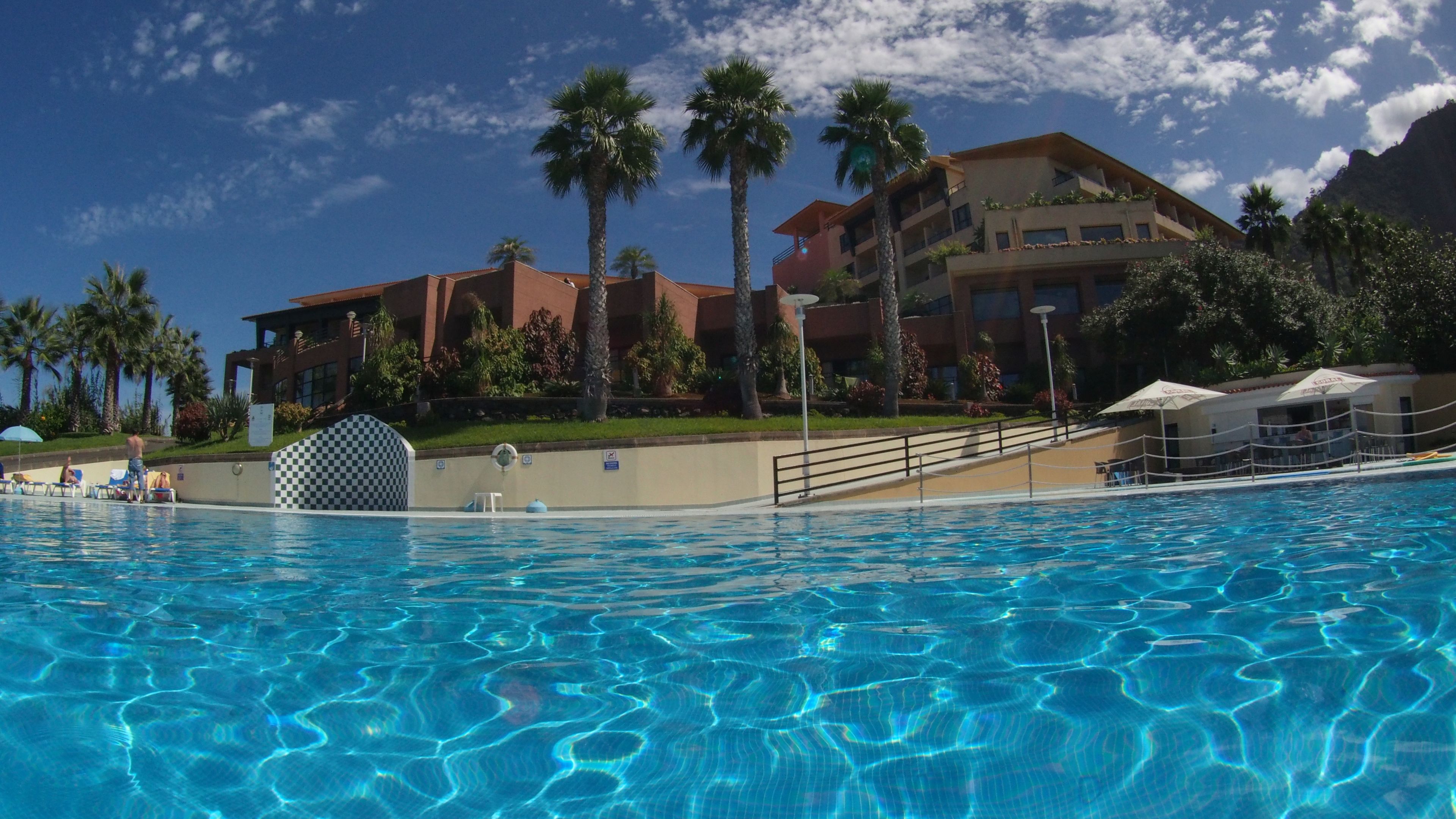 Una piscina con agua azul cristalina, rodeada de palmeras y un edificio con varios balcones.