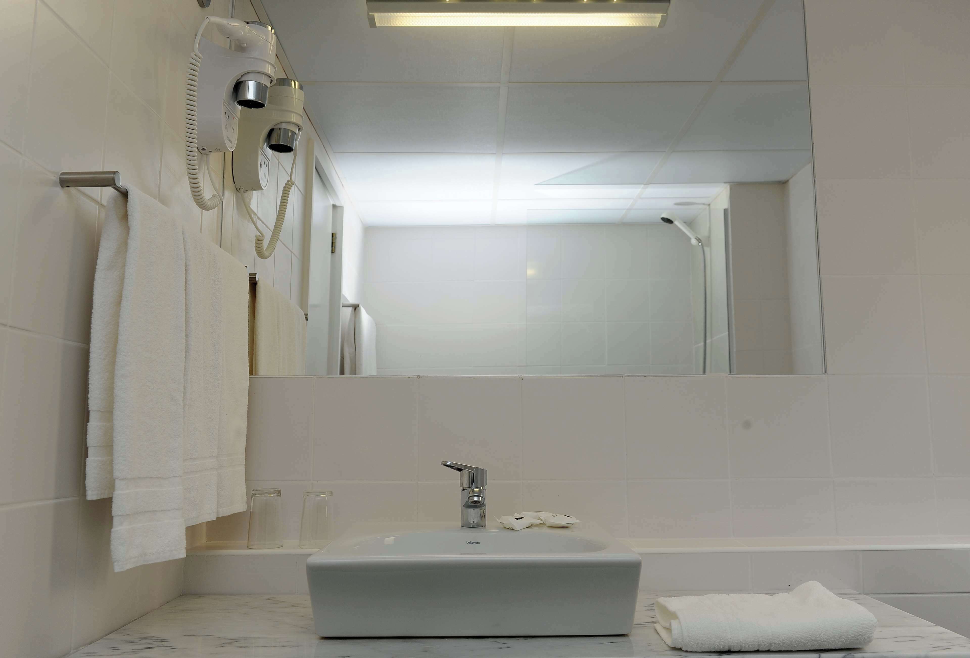 Un baño con un lavabo blanco, un cabezal de ducha de mano y un perchero para toallas.