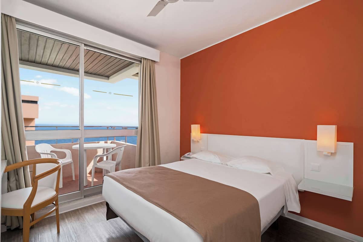 Ein Hotelzimmer mit Bett, Stuhl, Tisch und Meerblick.