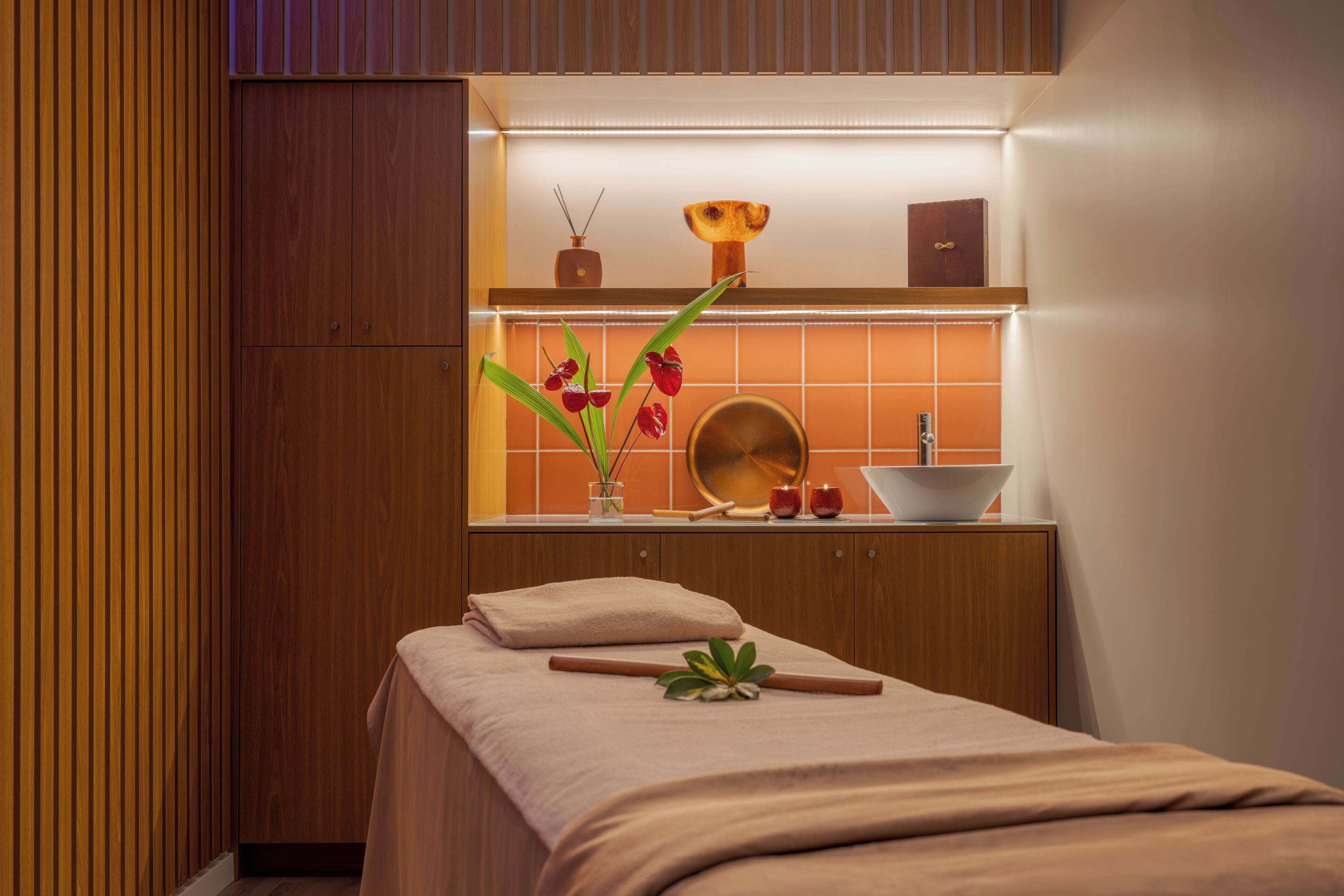 A modern bathroom with a wooden vanity, a mirror, a sink, and a towel on a bed.