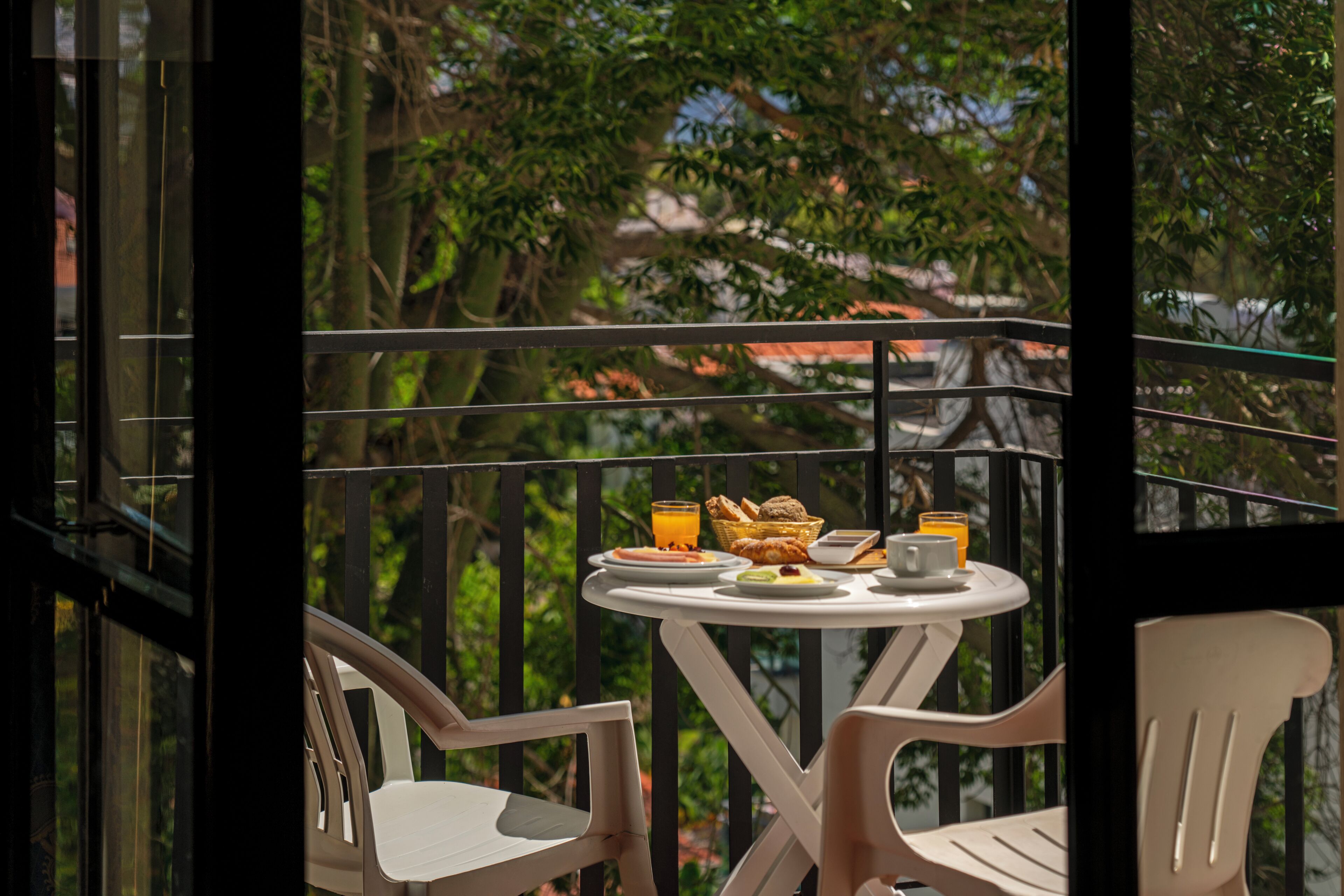 A balcony with a table set for breakfast, including plates, glasses, and a basket.