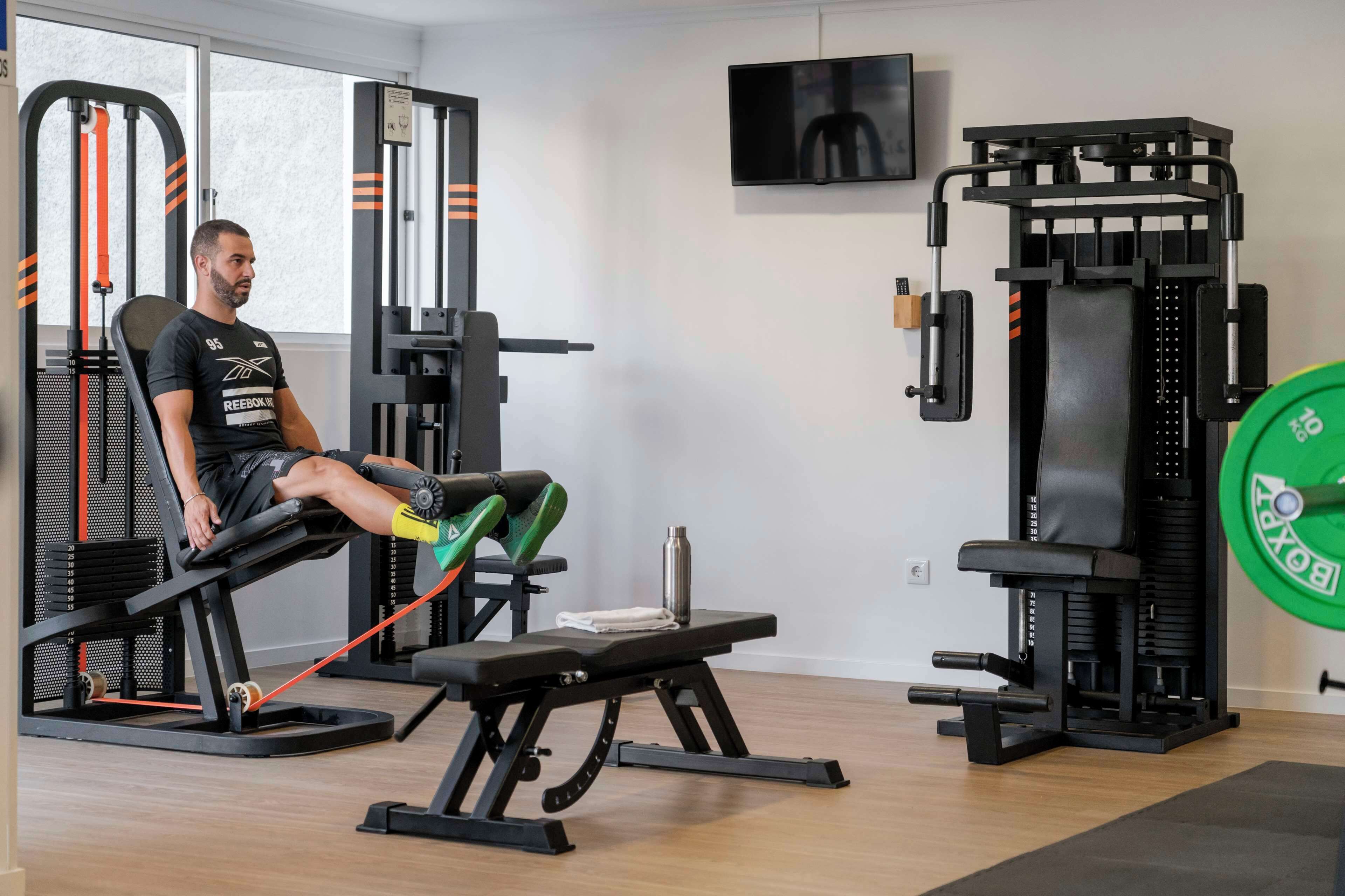 A gym with a bench press, weight racks, and a TV on the wall.