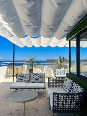 An outdoor seating area with white and black patterned furniture, a round metal table, and a view of the ocean. - Dorisol Mimosa Studio Hotel (Funchal)