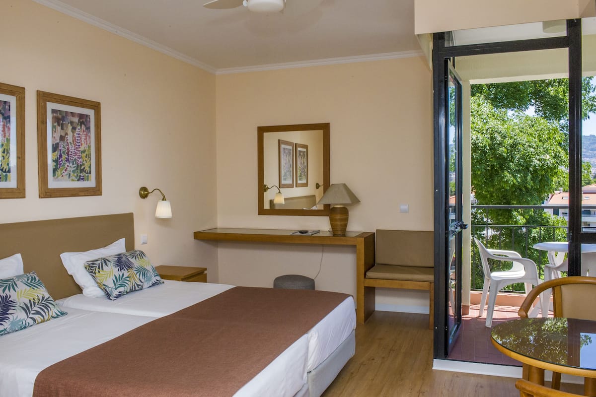 A hotel room with a bed, desk, chair, and balcony with outdoor furniture.