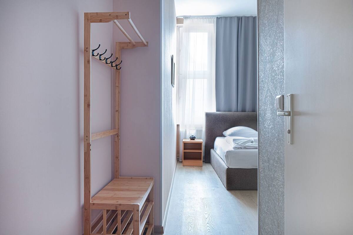 Ein Schlafzimmer mit einem Bett, einer hölzernen Bank, einem Kleiderständer und einer Tür zu einem weiteren Raum.