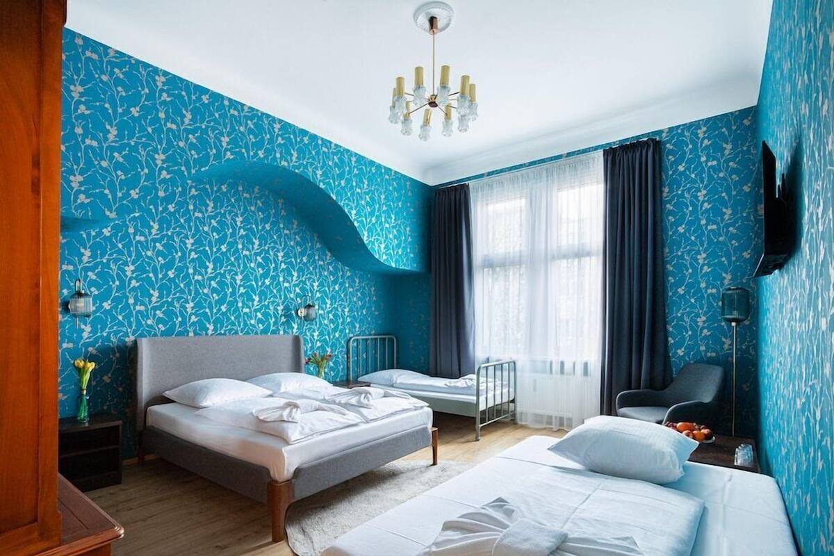Ein Hotelzimmer mit zwei Betten, einem Fernseher, einer Chandelierleuchtre und einem fenster mit Vorhängen.