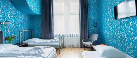 Un dormitorio con dos camas, una silla, un radiador y un televisor en la pared.