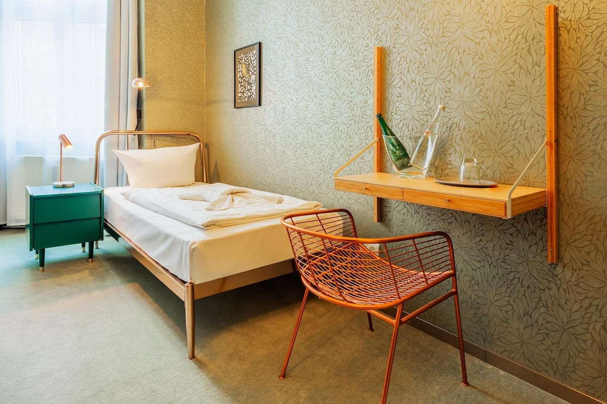 Ein ordentlich eingerichtetes Schlafzimmer mit einem Bett, einem Sessel, einem Nachttisch und einer Wandregal mit Dekoration.