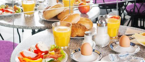 Mesa de café da manhã posta com pratos de comida, copos de suco de laranja e uma xícara de café.