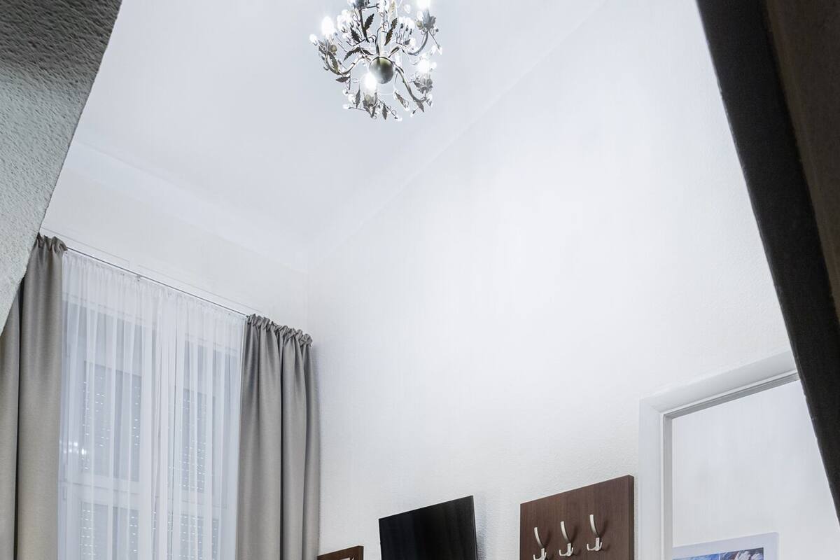Ein modernes Hotelzimmer mit einem großen Bett, einem kleinen Nachttisch mit Blumen in einer Vase, einem flachbildfernseher an der Wand und einem großen Spiegel.