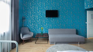 Una sala de estar con una pared verde azulada estampada, un sofá gris, un sillón gris, una mesa de centro y un televisor de pantalla plana montado en la pared.