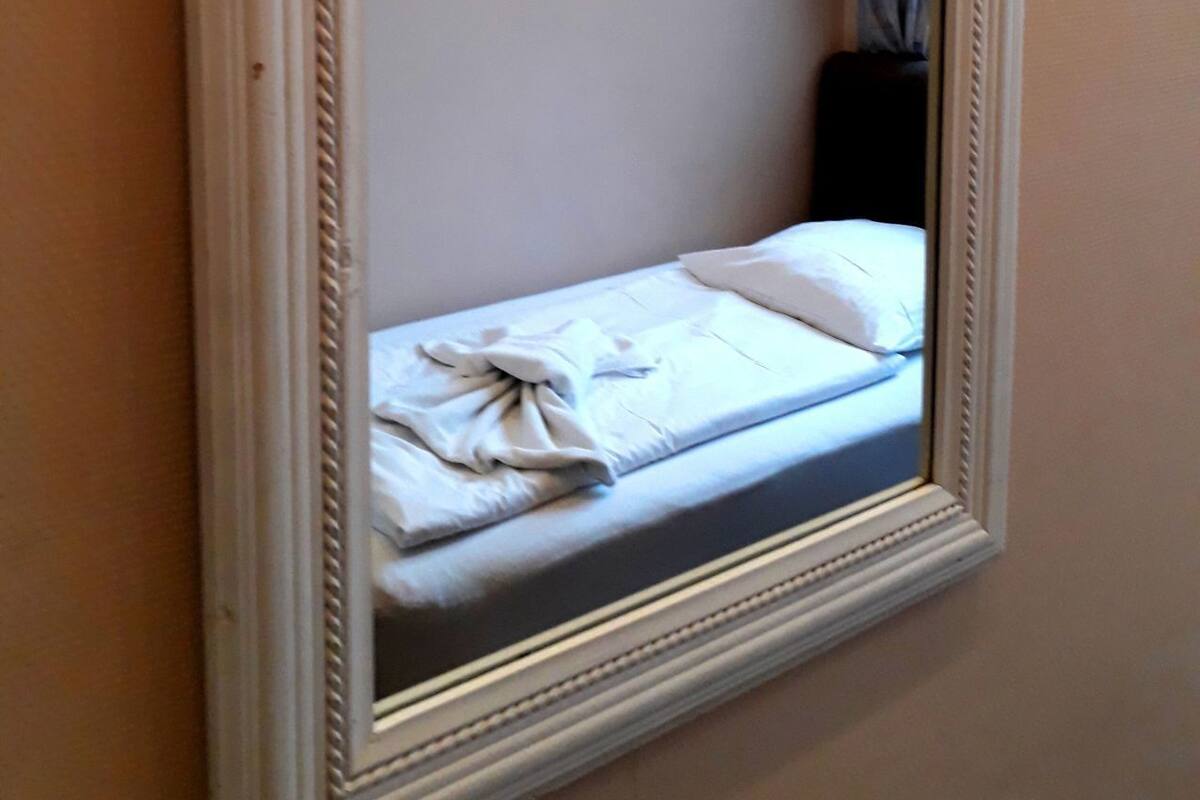Ein Spiegel mit weißem Rahmen, der ein Bett mit weißer Bettwäsche und einem Kopfkissen reflektiert.