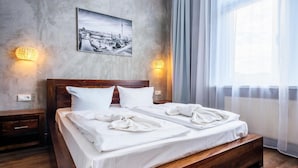Habitación de hotel con cama de madera, ropa de cama blanca, un cuadro de paisaje urbano y apliques de pared.