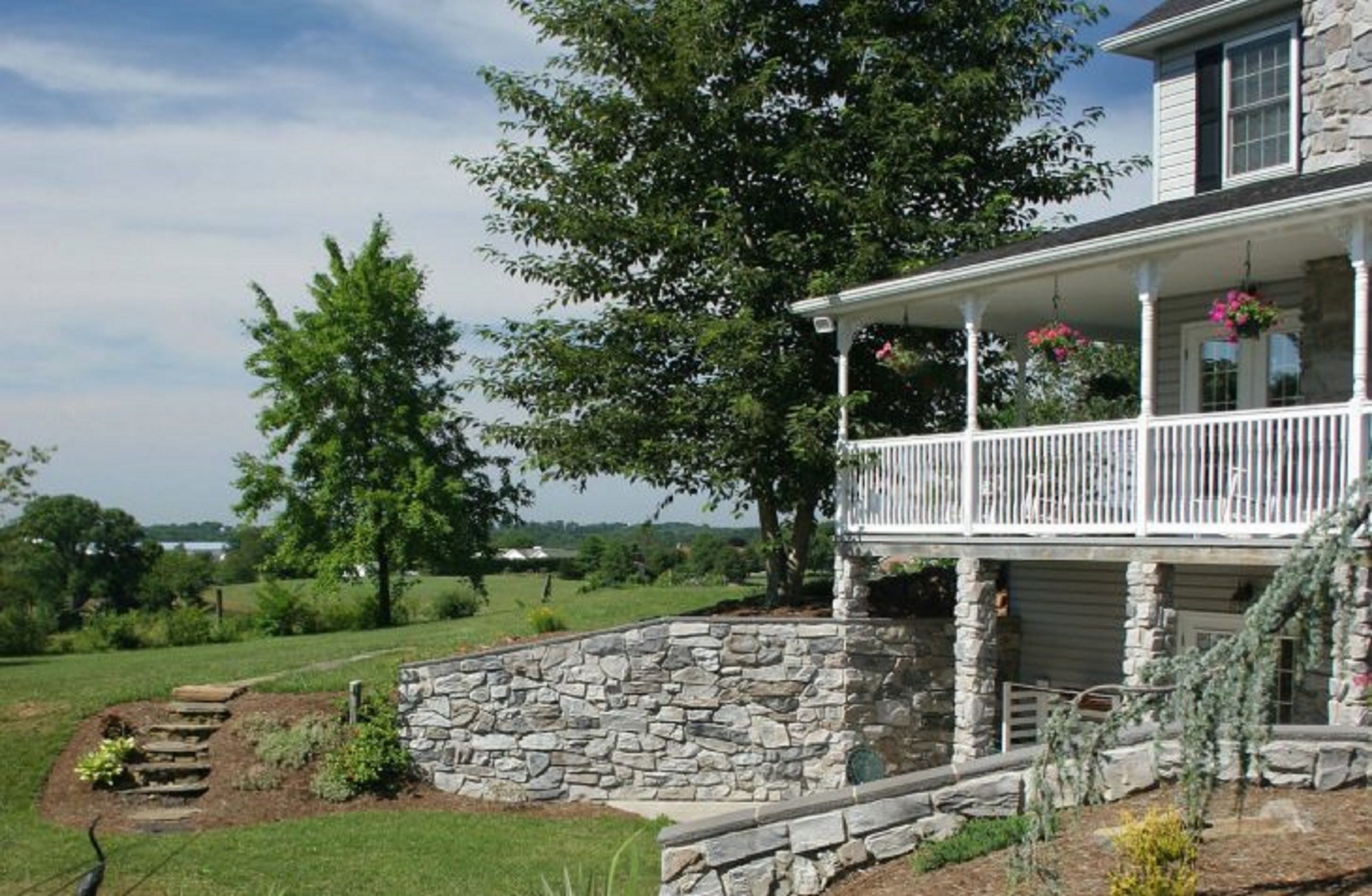 A two-story house with a stone foundation and a white porch with a railing.