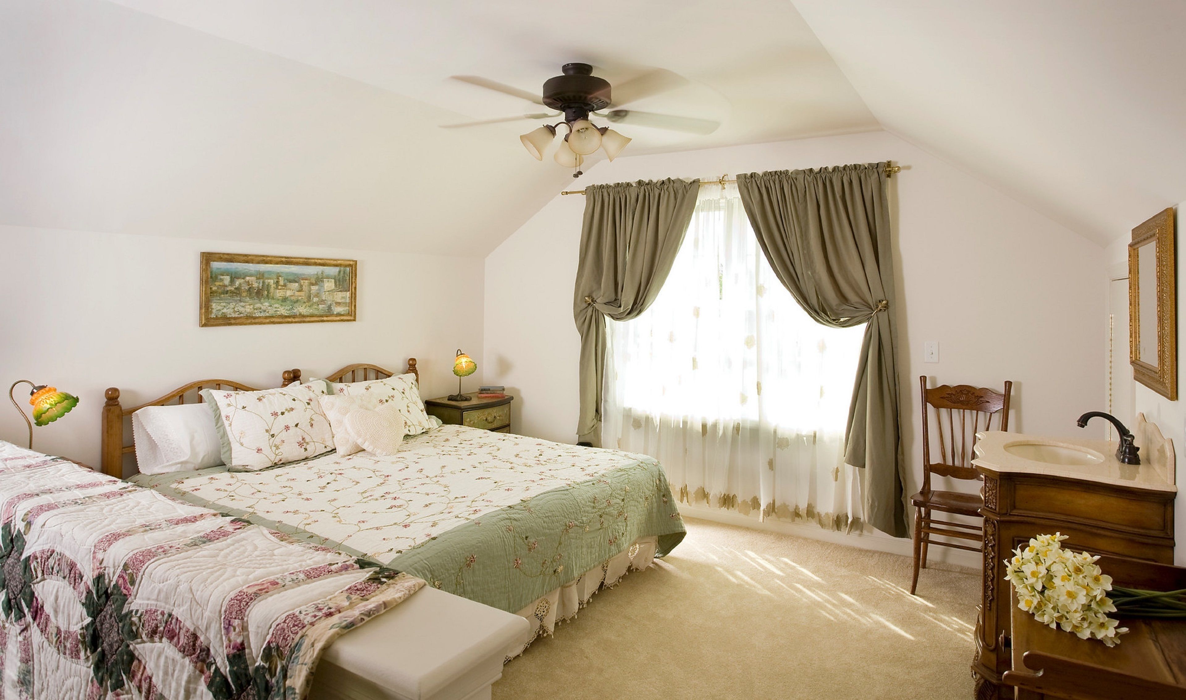 A bedroom with a bed, a nightstand, a desk with a mirror, and a window with curtains.
