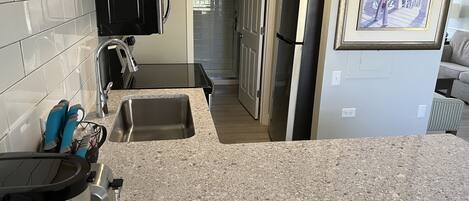 A kitchen with granite countertops, stainless steel appliances, and a view of the living area.