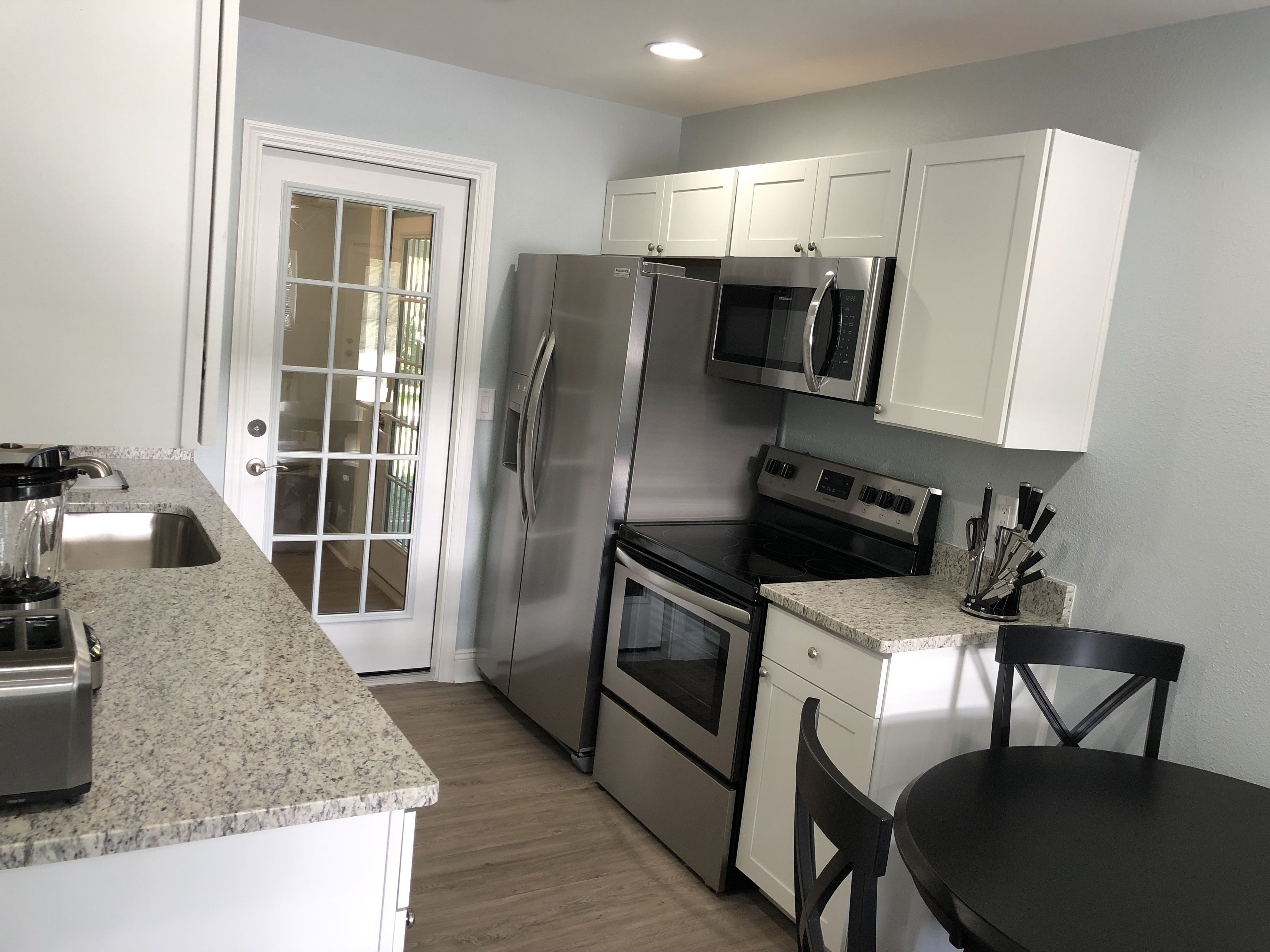 A kitchen with white cabinets, stainless steel appliances, a granite countertop, and a dining area with a black table and chairs.