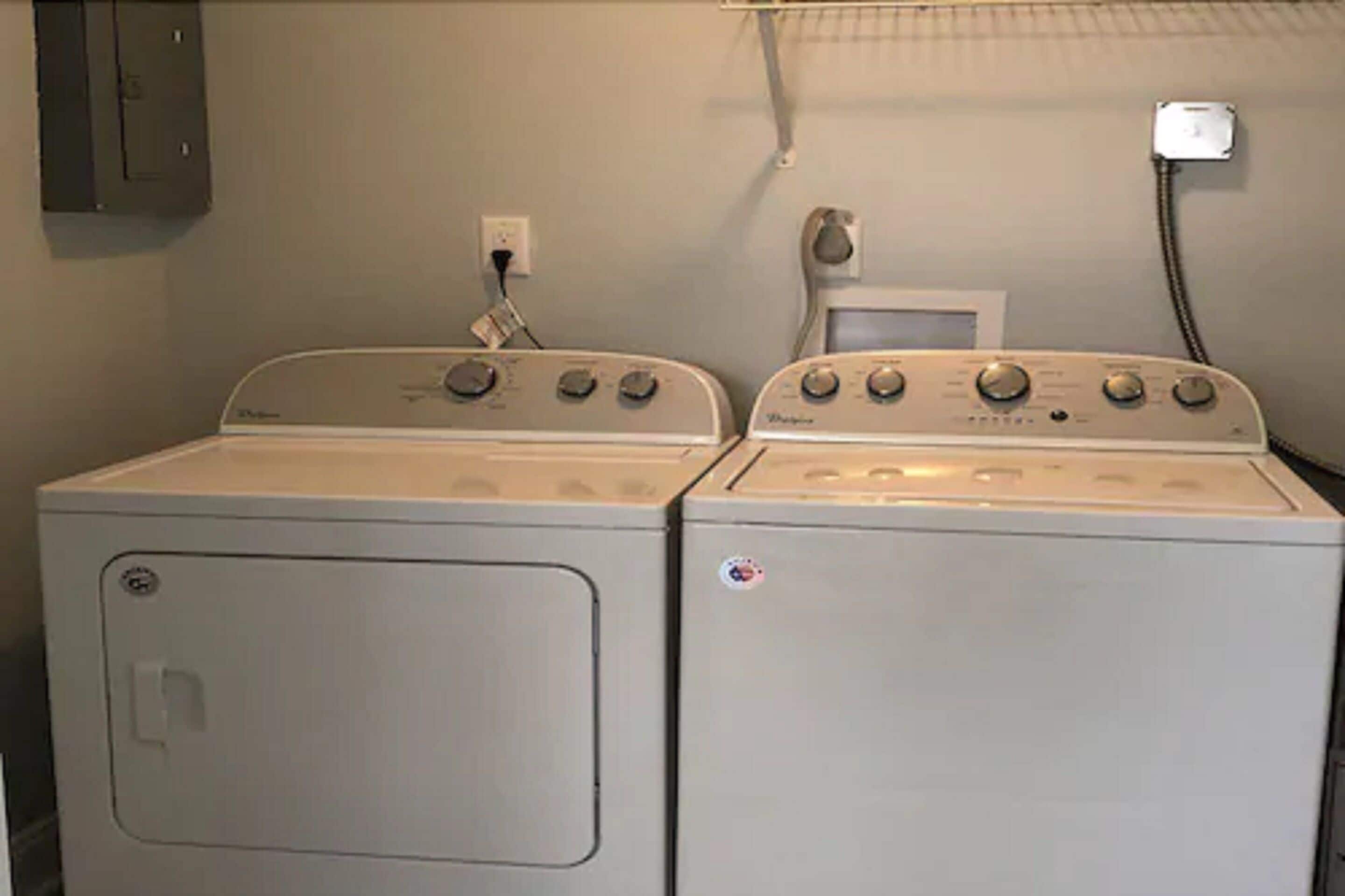 Twee witte wasmachines met een voorlaadklep, bedieningsknoppen en een stopcontact op de muur.