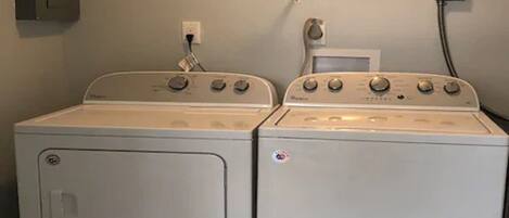 Twee witte wasmachines met een voorlaadklep, bedieningsknoppen en een stopcontact op de muur.