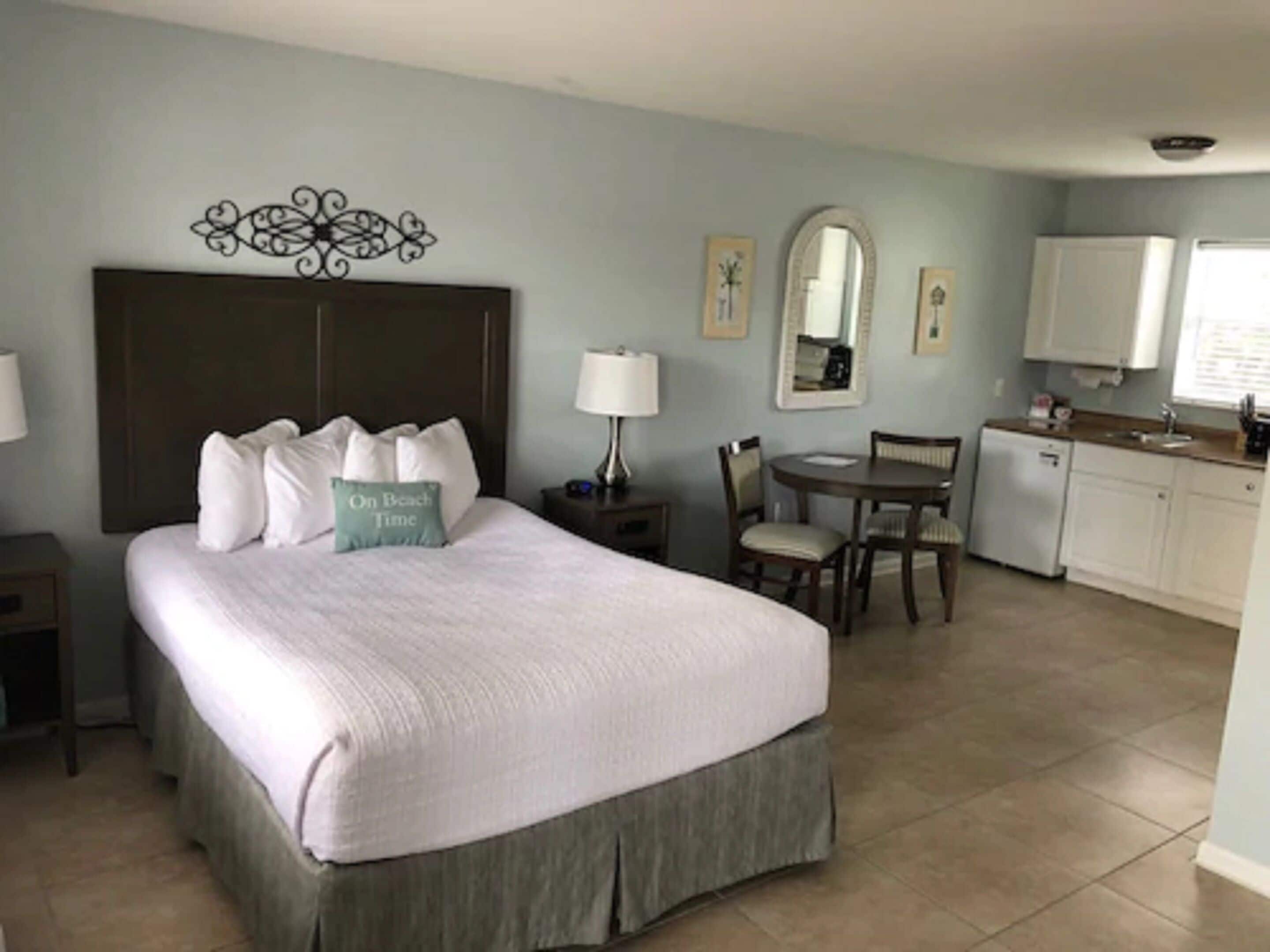 Una habitación de hotel con cama, escritorio, silla, kitchenette pequeña y baño.