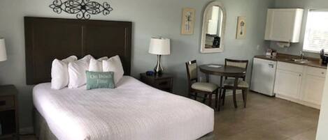 A hotel room with a bed, a desk, a chair, a small kitchenette, and a bathroom.