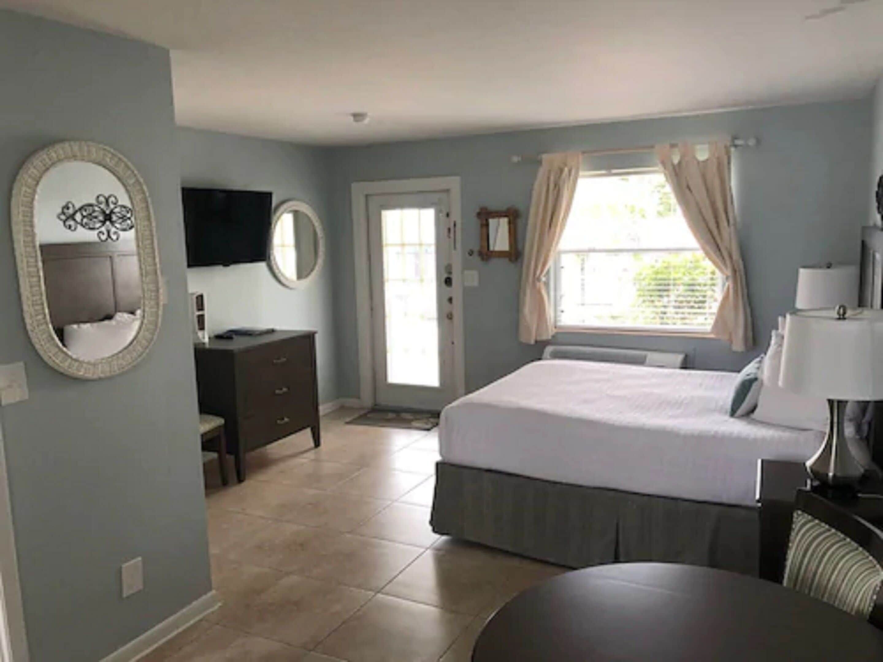 A bedroom with a bed, dresser, mirror, and a television on the wall.