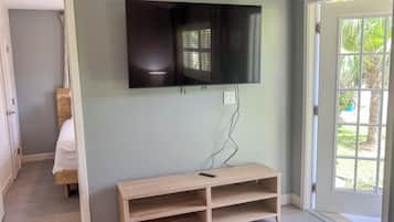 Une pièce avec un téléviseur fixé au mur, un banc en bois et une porte donnant sur l’extérieur.