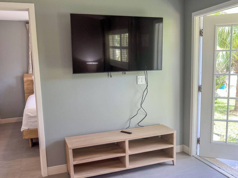 Una habitación con un televisor montado en la pared, un banco de madera y una puerta que da al exterior.