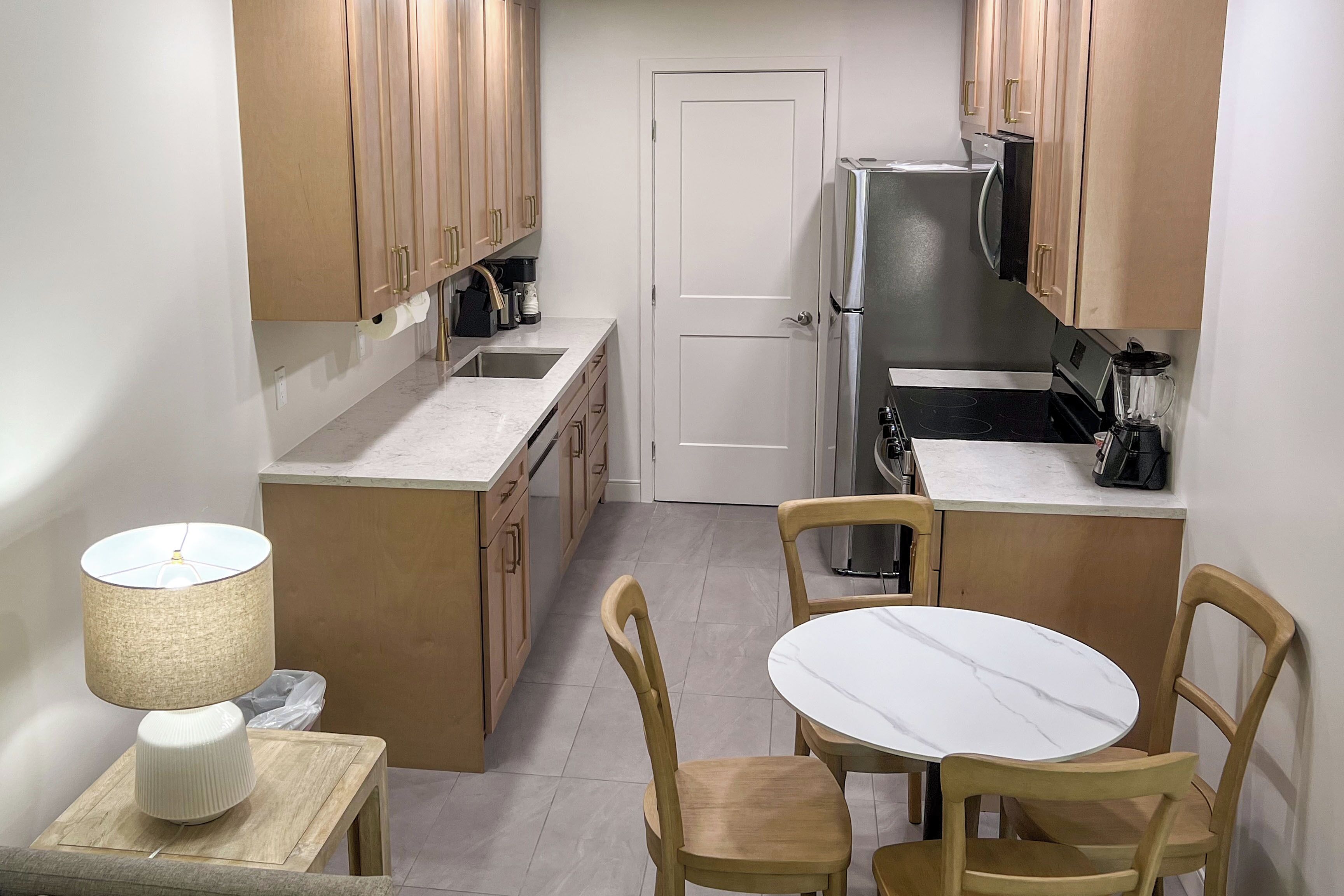 A compact kitchen with wooden cabinets, a white refrigerator, a sink, and a small dining table with chairs.
