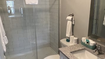 A modern bathroom with a glass-enclosed shower, a toilet, and a sink with a granite countertop.
