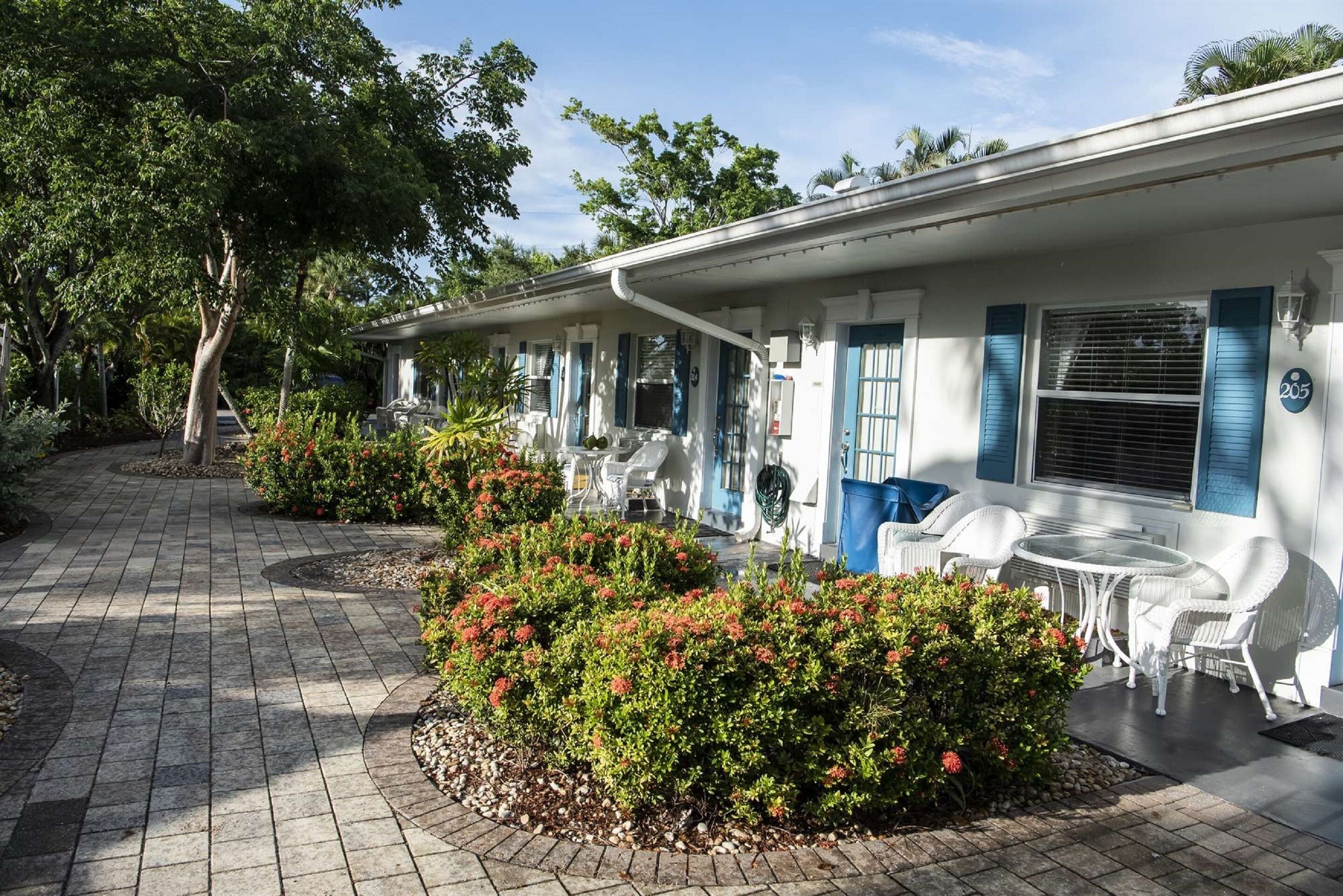 A row of white buildings with blue shutters, outdoor seating, and a paved walkway.
