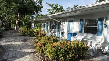 A row of white buildings with blue shutters, outdoor seating, and a paved walkway.