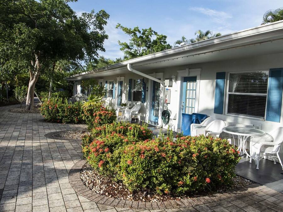 A row of white buildings with blue shutters, outdoor seating, and a paved walkway.