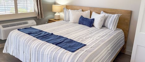 A neatly made bed with a striped bedspread and pillows, a bedside lamp, and an air conditioning unit.