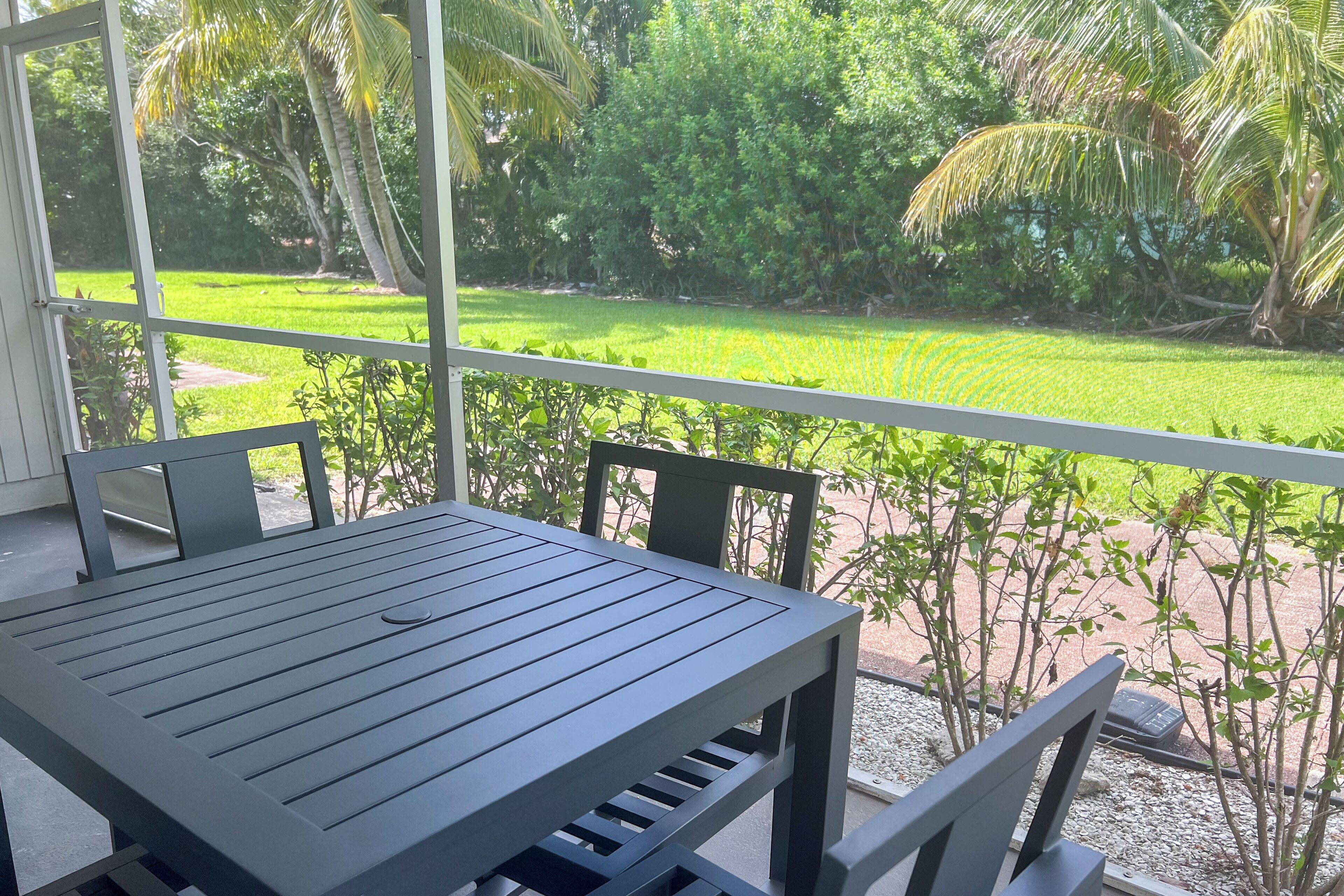 Un balcon avec une table et des chaises, donnant sur un jardin bien entretenu, agrémenté de palmiers et d’une pelouse.