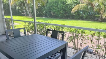 Un balcon avec une table et des chaises, donnant sur un jardin bien entretenu, agrémenté de palmiers et d’une pelouse.