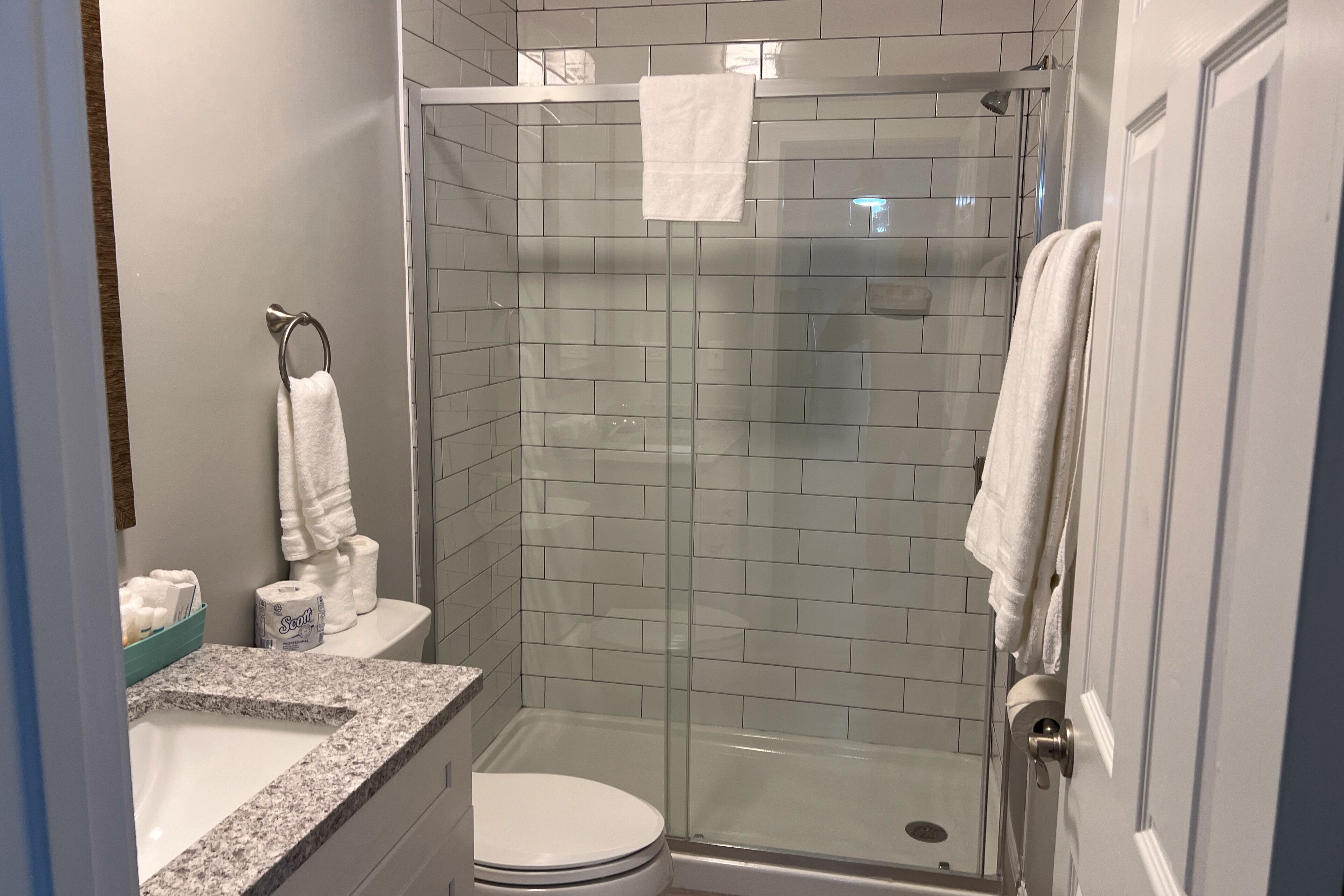 A bathroom with a glass-enclosed shower, a toilet, and a sink with a granite countertop.