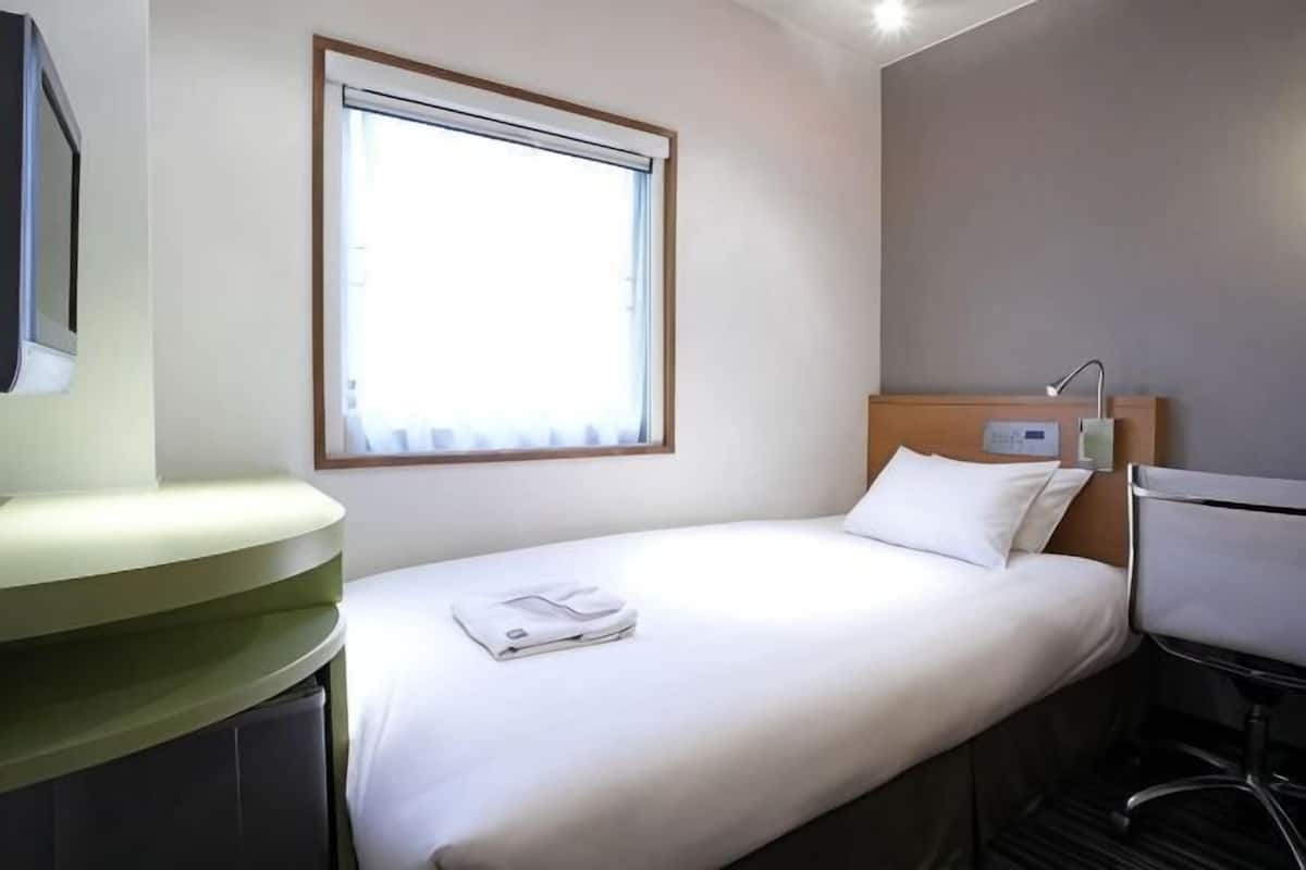 A hotel room with a bed, a bedside table, a window, and a wall-mounted TV.