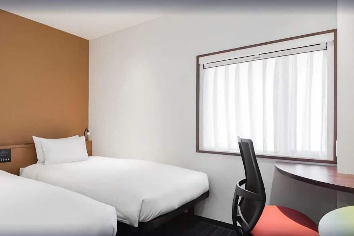 A hotel room with two beds, a desk, and a window with curtains.