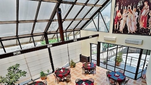 A spacious indoor area with a high ceiling and large windows, featuring multiple tables and chairs arranged for dining or socializing. - Cph Hotel Primavera (Tbilisi)