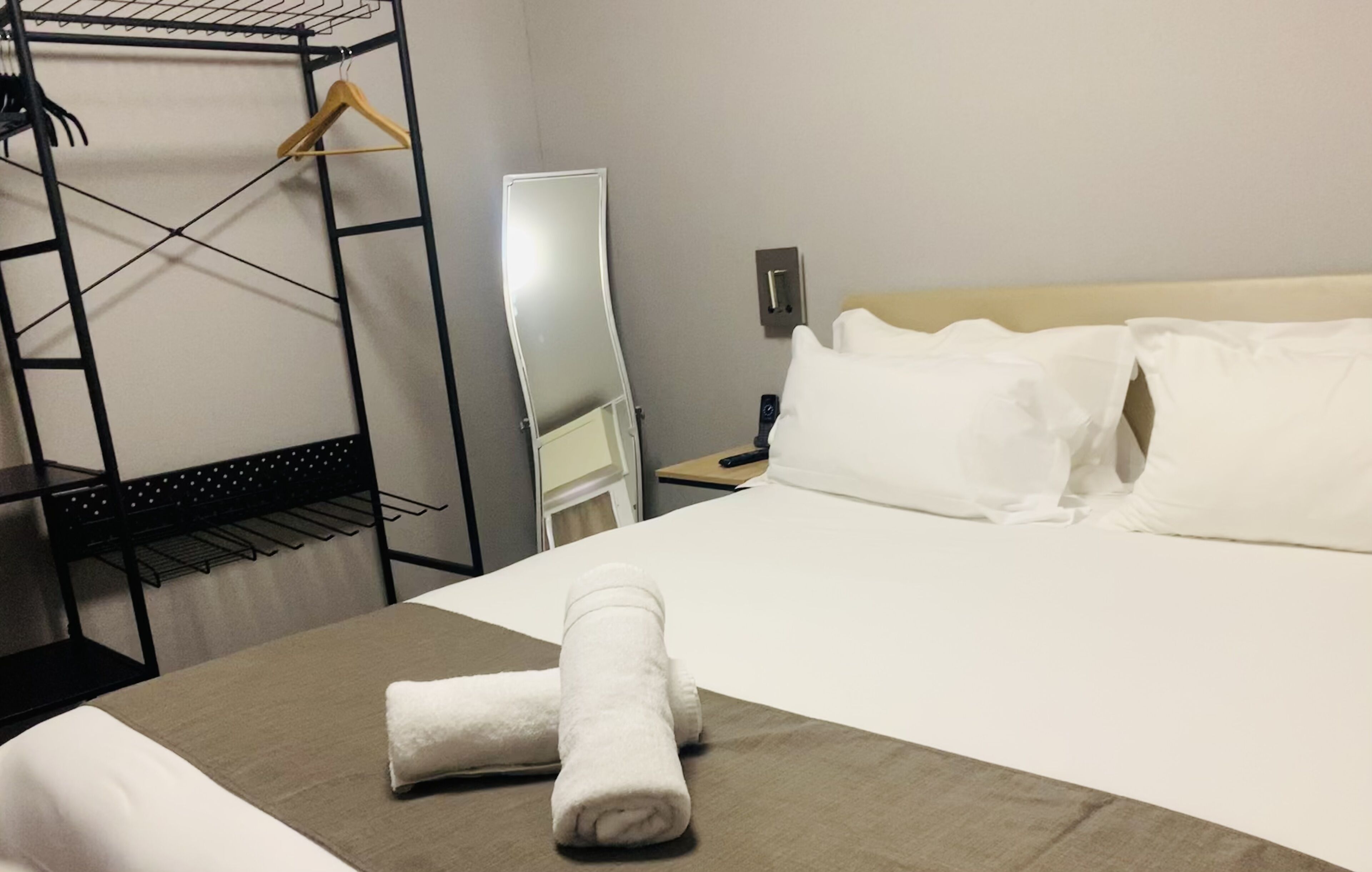 Una habitación de hotel con cama, armario, espejo y mesita de noche.