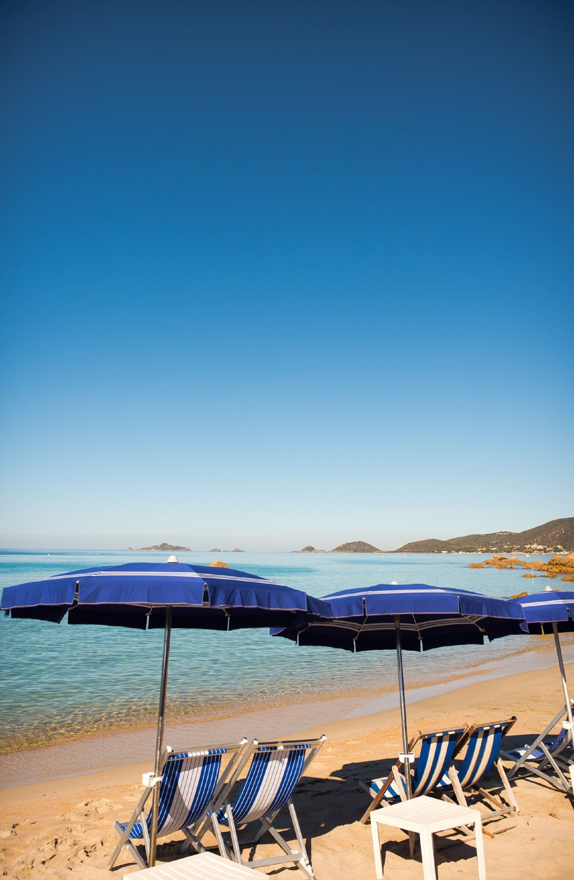 Una playa con sombrillas azules y sillas de playa a rayas.