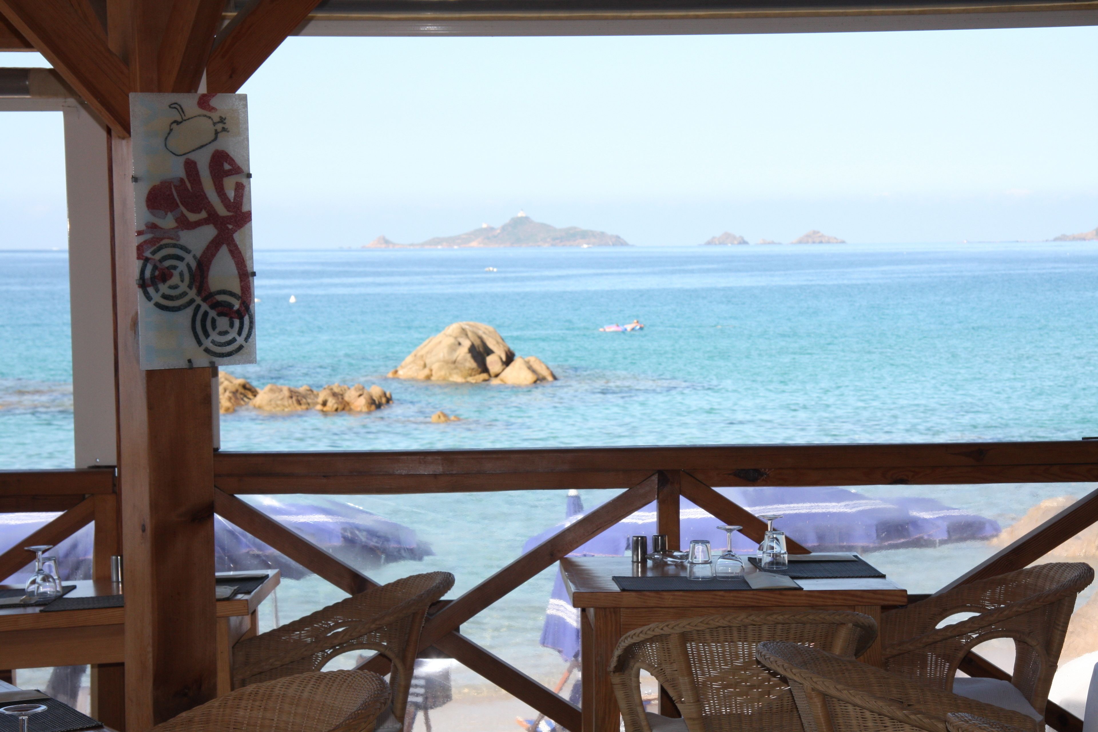 A seaside restaurant with wicker furniture, a view of the ocean, and a rocky outcrop.