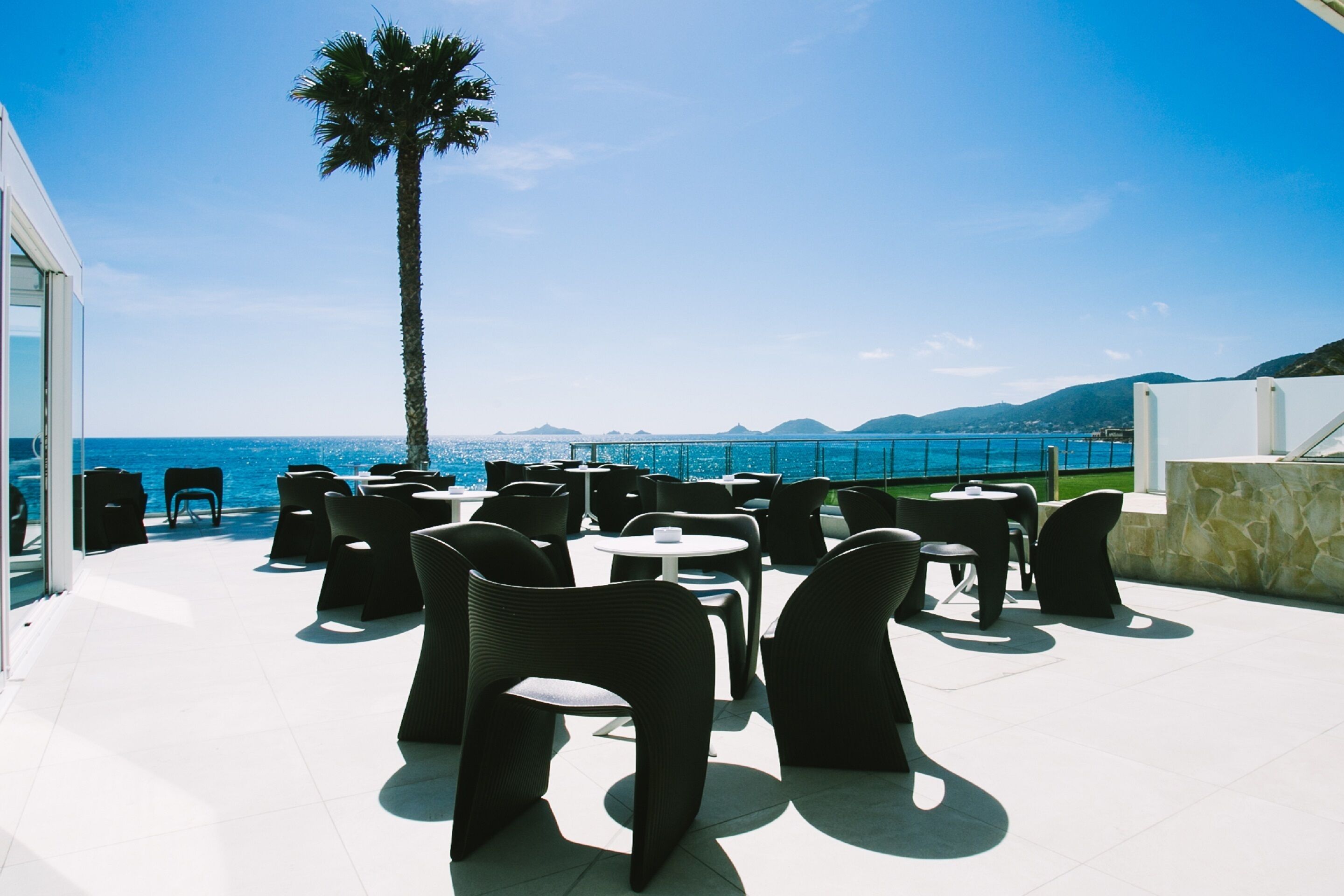 Terraza en la azotea con mobiliario exterior, una palmera y vistas al mar y las montañas.
