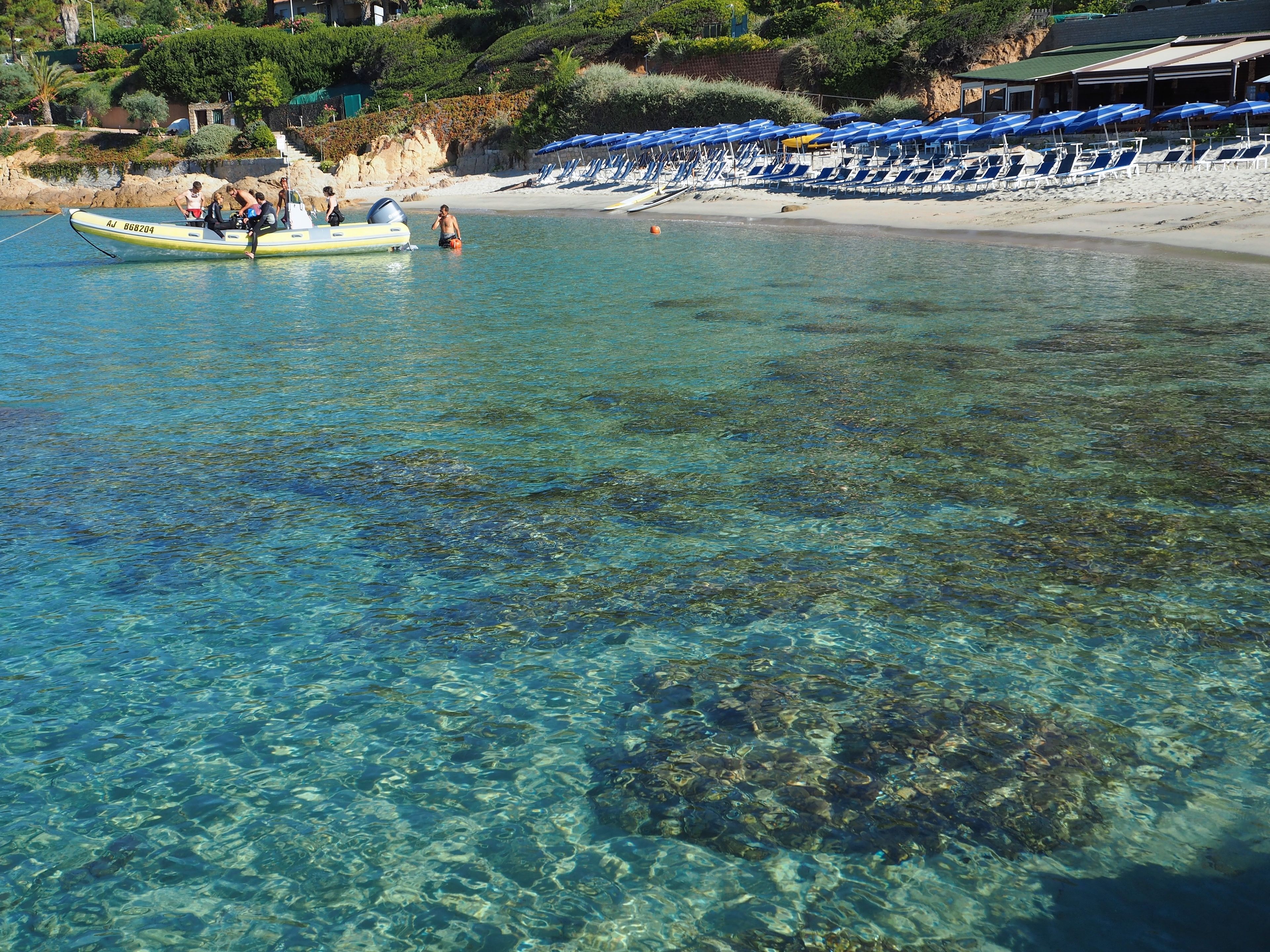 A clear beach with a boat and umbrellas.