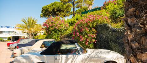 A white convertible car parked in a lot with a hotel in the background.