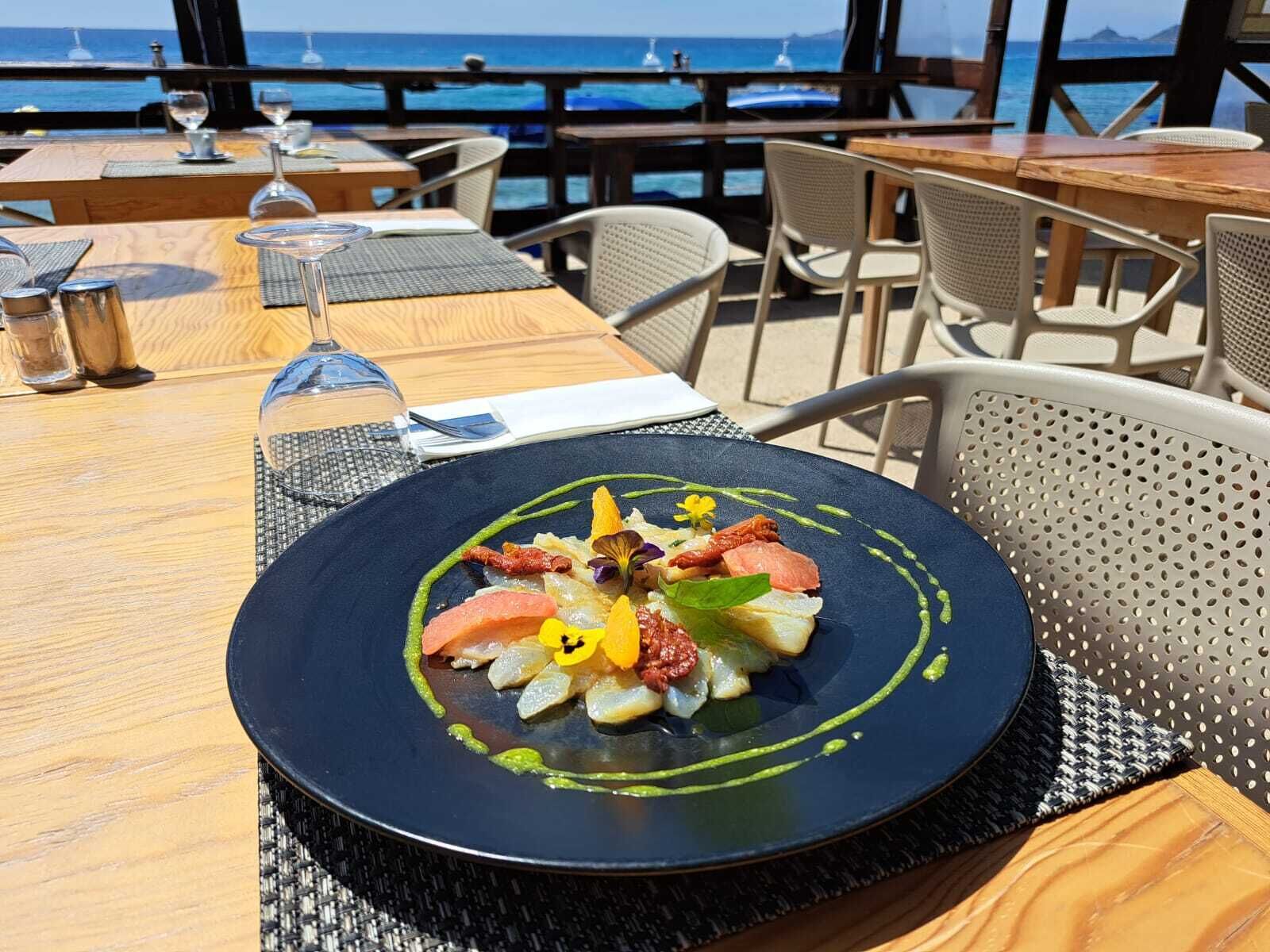A dining table with a plate of food, chairs, and a view of the ocean.