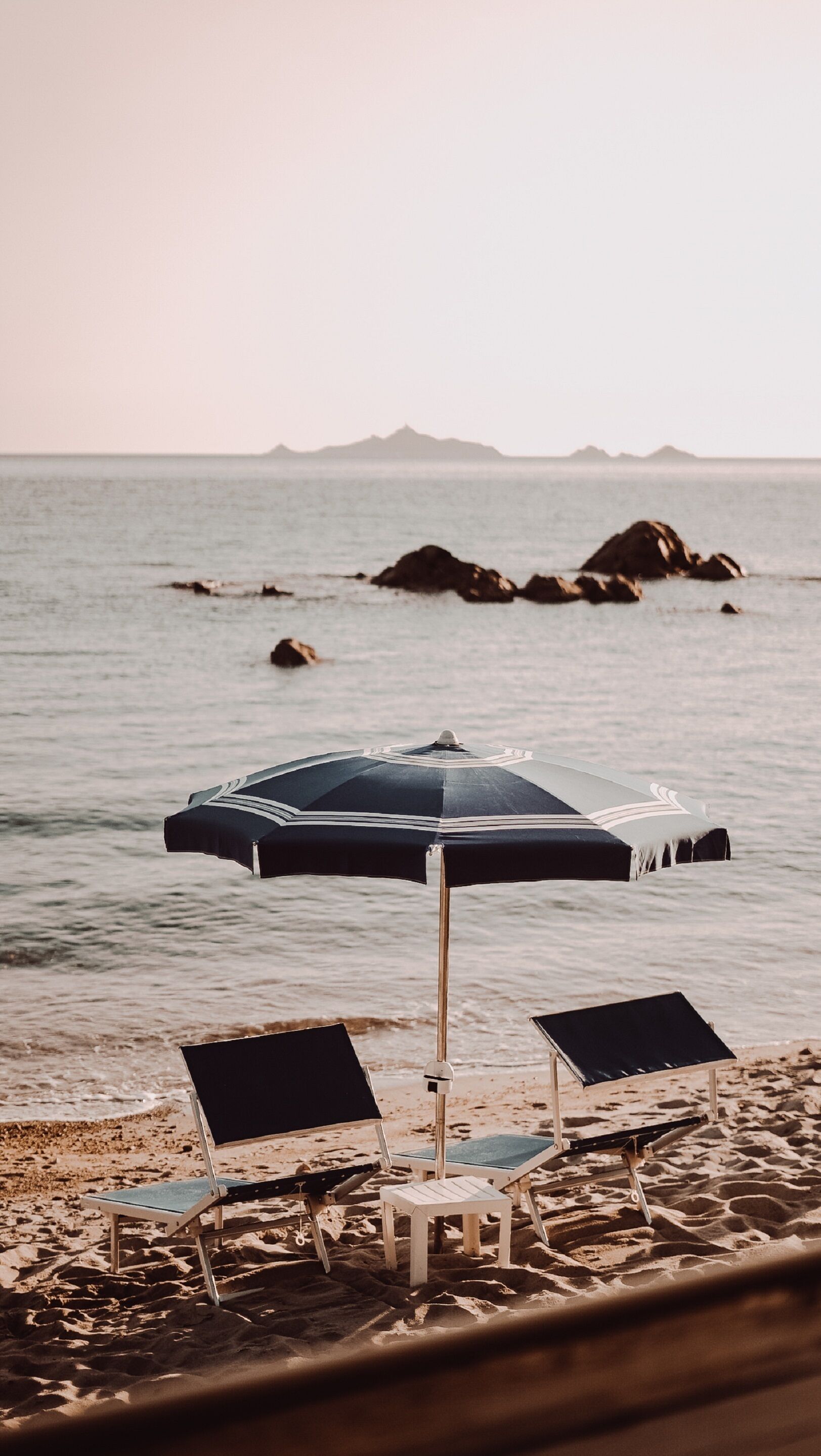 A beach with two lounge chairs and a single umbrella.