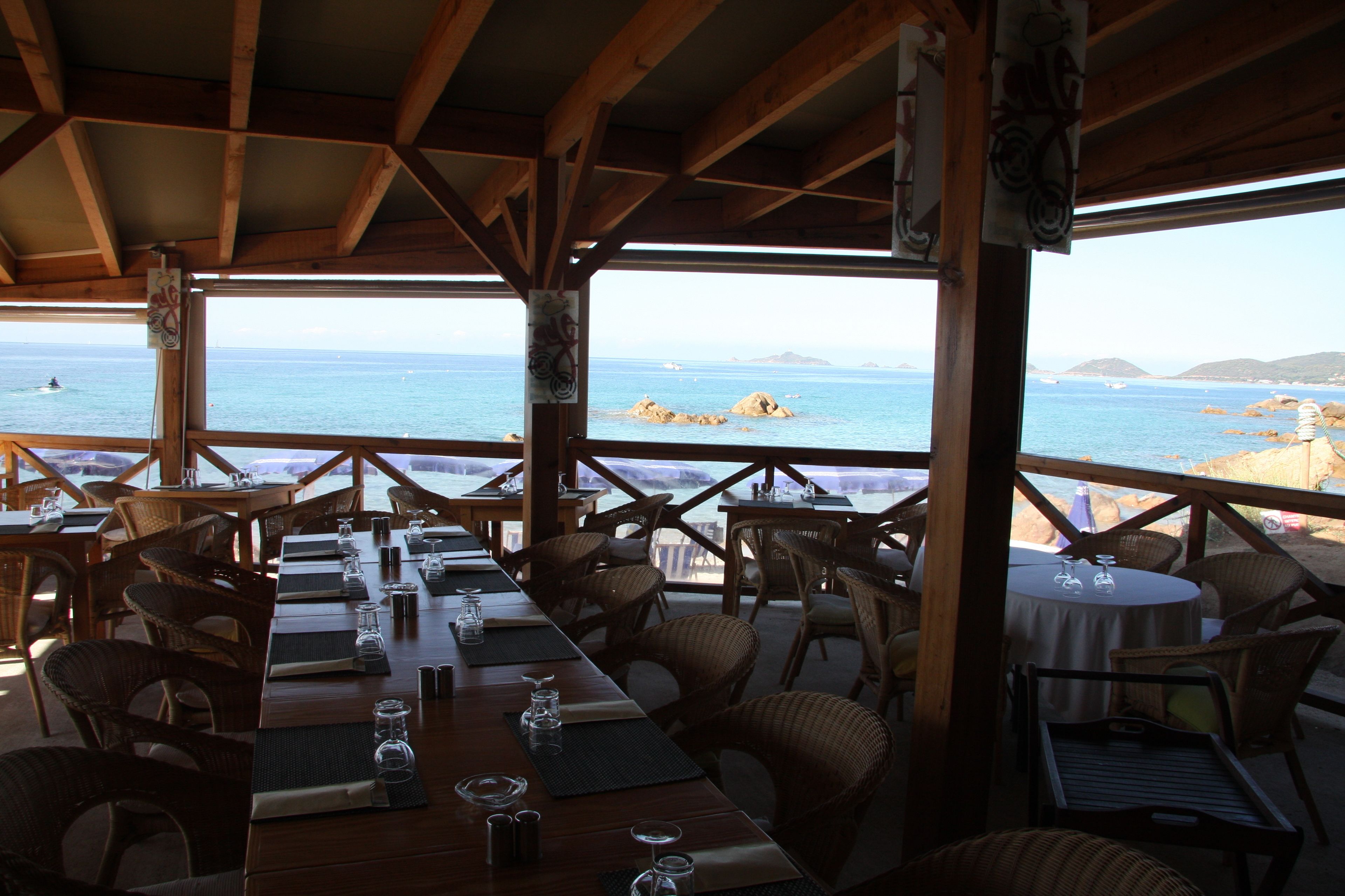 Un ristorante con tavoli e sedie in legno, affacciato su una costa rocciosa e il mare.