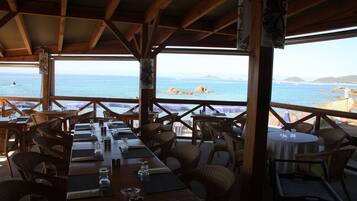 Un ristorante con tavoli e sedie in legno, affacciato su una costa rocciosa e il mare.
